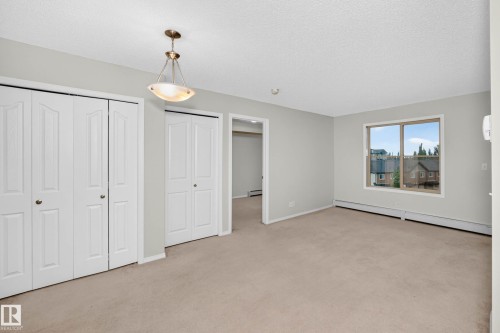 Spacious room featuring neutral carpeting, light gray walls, a window offering exterior views, and multiple white bi-fold closet doors - #404 12025 22 Av Sw, Edmonton, AB - Indoor Photo Showing Other Room