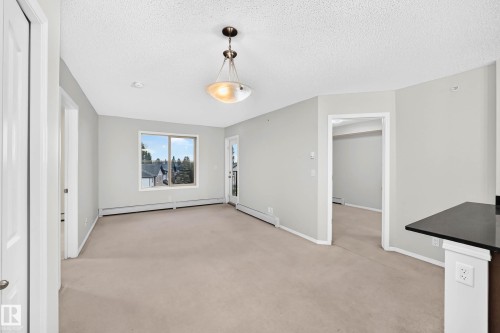 Open-concept living area featuring light gray walls, neutral carpeting, and a large window - #404 12025 22 Av Sw, Edmonton, AB - Indoor Photo Showing Other Room