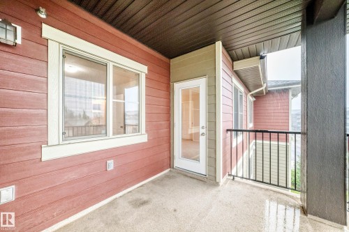 Outdoor balcony with concrete flooring, red siding, a white-framed window, and a white-framed glass paneled door - #404 12025 22 Av Sw, Edmonton, AB - Outdoor With Balcony With Exterior