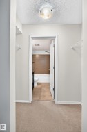 Hallway with neutral tone carpeting and white trim leading to a bathroom featuring a white bathtub, ceramic tile shower surround, and tile flooring - 