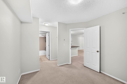 Carpeted room featuring light gray wall paint and white trim, with two doorways revealing additional interior spaces - #404 12025 22 Av Sw, Edmonton, AB - Indoor Photo Showing Other Room