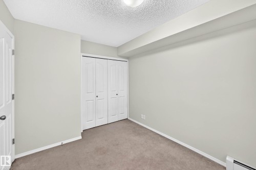 Carpeted room featuring a double bi-fold closet, light-toned walls, white trim, and a ceiling-mounted light fixture - #404 12025 22 Av Sw, Edmonton, AB - Indoor Photo Showing Other Room