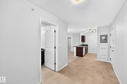 Entryway featuring tile flooring, leading to a kitchen with dark cabinetry and a light fixture - 