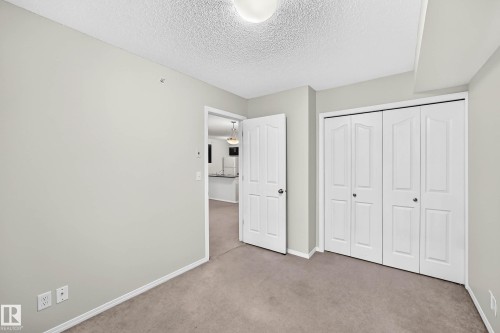 Neutral-toned wall paint with a textured ceiling, featuring a bi-fold closet door system - #404 12025 22 Av Sw, Edmonton, AB - Indoor