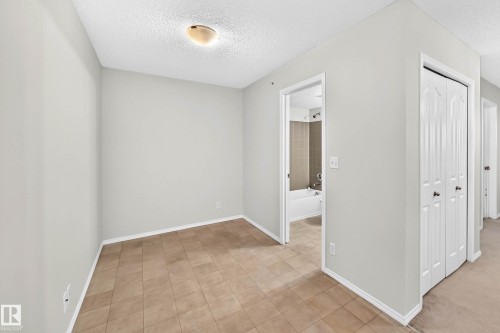 Room featuring light neutral walls, textured ceiling, flush mount ceiling light, and square tile flooring - #404 12025 22 Av Sw, Edmonton, AB - Indoor Photo Showing Other Room