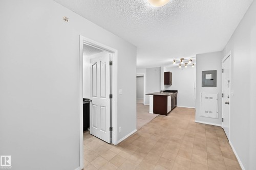 Entryway featuring tile flooring, leading to a kitchen with dark cabinetry and a light fixture - #404 12025 22 Av Sw, Edmonton, AB - Indoor Photo Showing Other Room