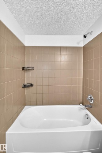 White bathtub with chrome fixtures, surrounded by light brown square wall tiles - #404 12025 22 Av Sw, Edmonton, AB - Indoor Photo Showing Bathroom