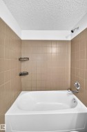 White bathtub with chrome fixtures, surrounded by light brown square wall tiles - 