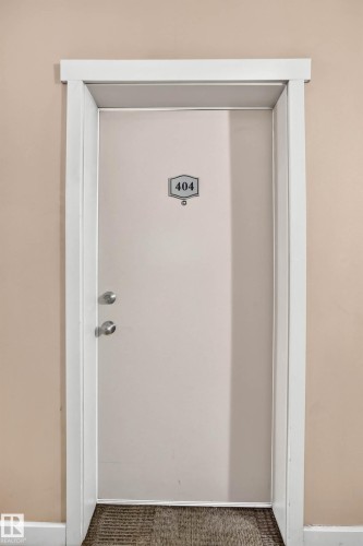 Entry door with white trim, brushed nickel hardware, and a number plate against a beige wall - #404 12025 22 Av Sw, Edmonton, AB - Indoor Photo Showing Other Room