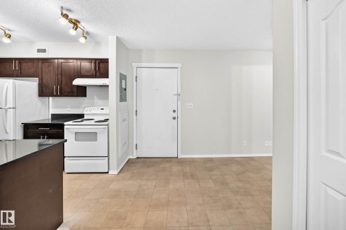 Kitchen featuring dark wood cabinetry, white appliances, and black countertops - #404 12025 22 Av Sw, Edmonton, AB - Indoor Photo Showing Kitchen