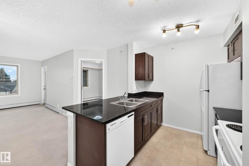 Kitchen featuring dark wood cabinetry, a dark countertop, and a double-basin stainless steel sink - #404 12025 22 Av Sw, Edmonton, AB - Indoor Photo Showing Kitchen With Double Sink