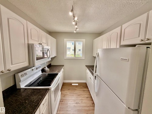 Galley kitchen featuring white cabinetry, dark speckled countertops, wood-finish flooring, and track lighting - 11430 139 Avenue Nw, Edmonton, AB - Indoor