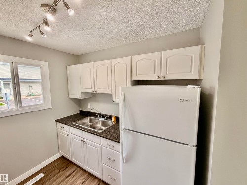 Kitchenette featuring white cabinetry, dark speckled countertops, a double stainless steel sink, and wood-finish flooring - 11430 139 Avenue Nw, Edmonton, AB - Indoor Photo Showing Kitchen With Double Sink