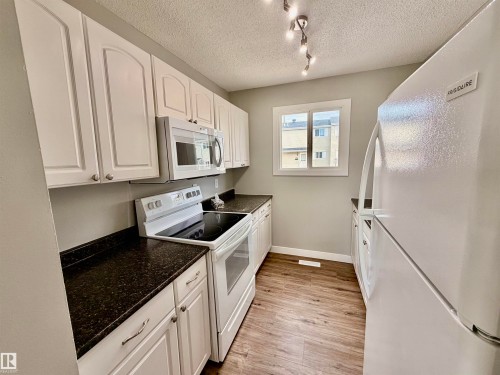 Kitchen featuring white cabinetry, dark speckled countertops, white appliances, wood-finish flooring, and a window - 11430 139 Avenue Nw, Edmonton, AB - Indoor Photo Showing Kitchen