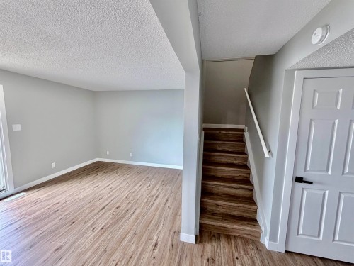Interior space featuring wood-finish flooring, light gray wall paint, white baseboards, and a staircase with matching wood-finish treads - 11430 139 Avenue Nw, Edmonton, AB - Indoor Photo Showing Other Room