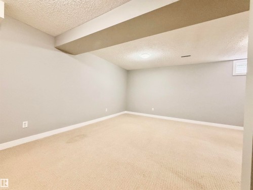 Spacious room featuring neutral carpeting, light gray walls, a textured ceiling, and an overhead light fixture - 11430 139 Avenue Nw, Edmonton, AB - Indoor Photo Showing Other Room