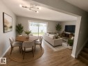 Open-concept living area with wood-finish flooring, a contemporary linear chandelier, and sliding glass doors opening to a paved patio - 11430 139 Avenue Nw, Edmonton, AB 