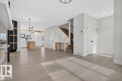 Spacious interior featuring light wood-finish flooring, a contemporary kitchen with an island, a modern chandelier, a built-in desk area, and a staircase with wood railing - 