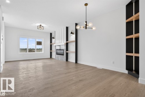 Spacious room featuring wood-finish flooring, a modern fireplace with a stone surround, and built-in shelving with integrated lighting - 43 River Birch Way, St. Albert, AB - Indoor
