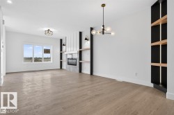 Spacious room featuring wood-finish flooring, a modern fireplace with a stone surround, and built-in shelving with integrated lighting - 