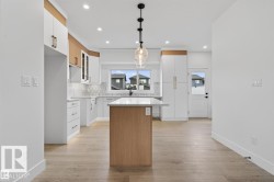 Modern kitchen featuring wood-finish flooring, a central island with a quartz countertop, and a contemporary pendant light fixture - 