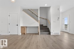 Open concept interior featuring wide plank wood-finish flooring, a built-in desk with natural wood cabinetry, and a carpeted staircase with light wood handrails - 
