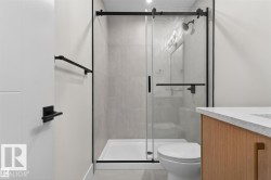 Contemporary bathroom featuring a glass-enclosed shower with matte black hardware, light-toned wall tiling, and a white shower pan - 