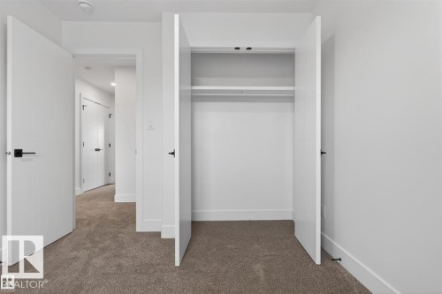 Carpeted interior space featuring a double-door closet with shelving and hanging rod, bright white walls, and contemporary black door hardware - 43 River Birch Way, St. Albert, AB - Indoor Photo Showing Other Room