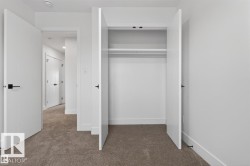 Carpeted interior space featuring a double-door closet with shelving and hanging rod, bright white walls, and contemporary black door hardware - 
