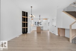 Open-concept living space featuring light wood-finish flooring, a built-in shelving unit with dark paneling, and contemporary lighting fixtures - 