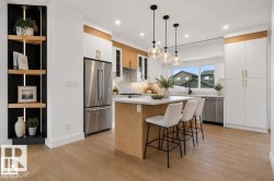 Bright kitchen featuring a central island with seating, stainless steel appliances, white cabinetry with gold-toned hardware, and wood-finish flooring - 