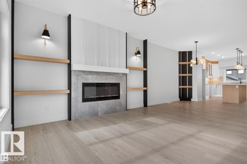 Living space featuring a linear electric fireplace with a textured surround, integrated wood-finish shelving, and light wood-finish flooring - 43 River Birch Way, St. Albert, AB - Indoor Photo Showing Living Room With Fireplace