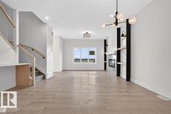 Open-concept living area featuring wood-finish flooring, a contemporary fireplace with mantel, and built-in shelving - 