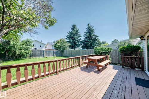 Expansive wood deck with decorative railings and a spacious backyard featuring a manicured lawn, mature trees, and privacy fencing - 6208 11 Ave Nw Nw, Edmonton, AB - Outdoor With Deck Patio Veranda With Exterior