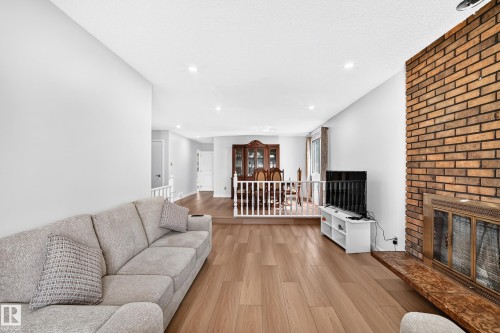Spacious living area featuring wood-finish flooring, recessed lighting, and a prominent brick fireplace with a brass fire screen - 6208 11 Ave Nw Nw, Edmonton, AB - Indoor Photo Showing Living Room With Fireplace