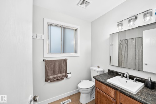 Bathroom featuring a single vanity with a white rectangular sink, dark patterned countertop, and wood-finish cabinetry - 6208 11 Ave Nw Nw, Edmonton, AB - Indoor Photo Showing Bathroom
