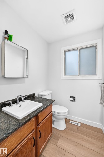 Bathroom featuring a wood-finish vanity with a built-in sink, dark stone-finish countertop, and chrome faucet - 6208 11 Ave Nw Nw, Edmonton, AB - Indoor Photo Showing Bathroom