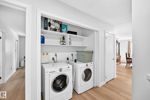 Dedicated laundry closet featuring a stacked washer and dryer, built-in shelving, and wood-finish flooring - 6208 11 Ave Nw Nw, Edmonton, AB - Indoor Photo Showing Laundry Room