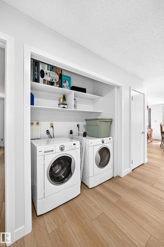Dedicated laundry area featuring a front-loading washer and dryer, integrated shelving, and wood-finish flooring - 6208 11 Ave Nw Nw, Edmonton, AB - Indoor Photo Showing Laundry Room