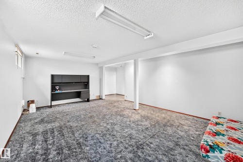 Lower-level room featuring gray patterned carpeting, white walls, and exposed ceiling beams - 6208 11 Ave Nw Nw, Edmonton, AB - Indoor
