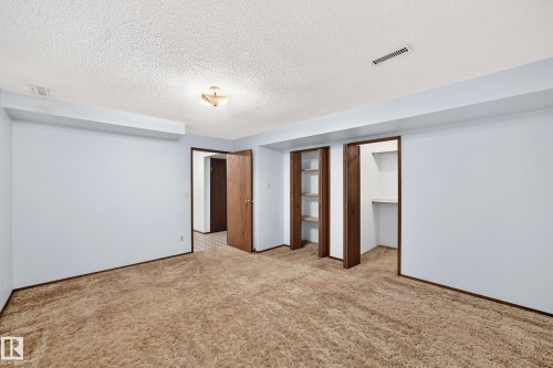 Spacious room featuring light blue walls, brown carpet flooring, and two integrated closet spaces with wood-finish shelving - 6208 11 Ave Nw Nw, Edmonton, AB - Indoor Photo Showing Other Room