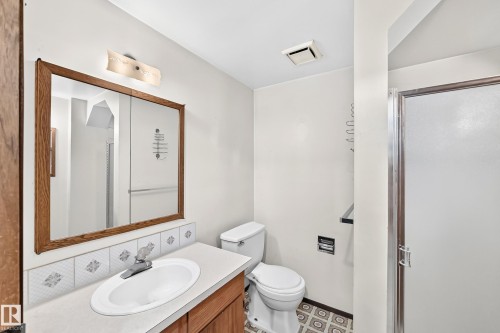Bathroom featuring a wood-framed medicine cabinet, a single vanity with a white countertop and oval sink, decorative tile backsplash, and a shower with a frosted glass door - 6208 11 Ave Nw Nw, Edmonton, AB - Indoor Photo Showing Bathroom