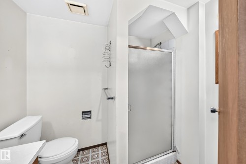 Bathroom featuring a shower stall with a frosted glass door, a white toilet, and patterned floor tiles - 6208 11 Ave Nw Nw, Edmonton, AB - Indoor Photo Showing Bathroom