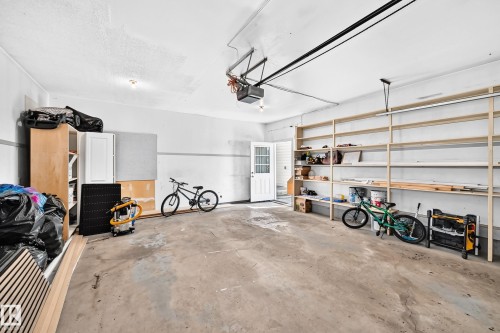 Spacious garage featuring a concrete floor, overhead lighting, an automatic garage door opener, extensive built-in shelving, and a side entry door with window panes - 6208 11 Ave Nw Nw, Edmonton, AB - Indoor Photo Showing Garage