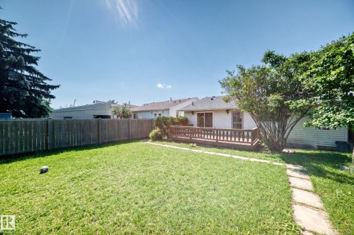 Expansive backyard featuring a manicured lawn, a wooden privacy fence, a wood deck, mature landscaping, and a stepping stone pathway - 6208 11 Ave Nw Nw, Edmonton, AB - Outdoor With Deck Patio Veranda