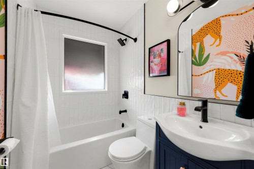 Bathroom featuring a built-in tub with shower, white subway tile surround, matte black fixtures, a contemporary vanity with an integrated sink, and an arched mirror - 10732 129 Street Nw, Edmonton, AB - Indoor Photo Showing Bathroom