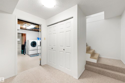 White bi-fold doors with black hardware, neutral carpeted flooring, and a partial staircase with wood-finish risers - 10732 129 Street Nw, Edmonton, AB - Indoor Photo Showing Other Room