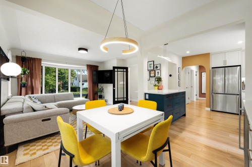 Open-concept living space featuring wood-finish flooring, a contemporary kitchen island with a light-toned countertop, stainless steel appliances, and a curved bay window - 10732 129 Street Nw, Edmonton, AB - Indoor Photo Showing Dining Room