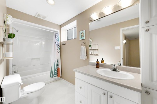 Bathroom featuring a white bathtub with an integrated shower, a vanity with a white countertop and oval sink, a large wall-mounted mirror, and white cabinetry with brushed nickel hardware - 10732 129 Street Nw, Edmonton, AB - Indoor Photo Showing Bathroom
