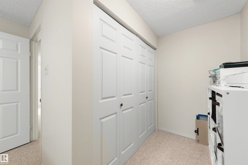 Hallway featuring a neutral color palette, paneled closet doors, and textured wall-to-wall carpeting - 10732 129 Street Nw, Edmonton, AB - Indoor Photo Showing Other Room